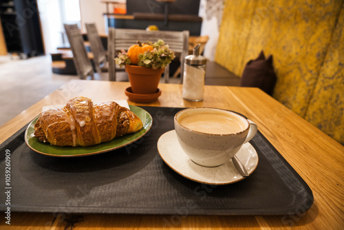 A white cup of cappuccino, a spoon, a croissant, a sugar bowl on a table in a café. Selective focus, shallow depth of field. photo