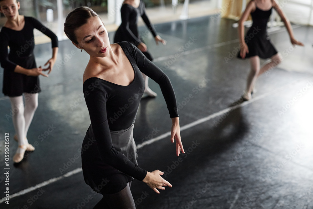 Side view of female dance teacher in black leotard gracefully moving practicing ballet positions while teaching little kids in studio, copy space Side view of female dance teacher in black leotard gracefully moving practicing ballet positions while teaching little kids in studio, copy space