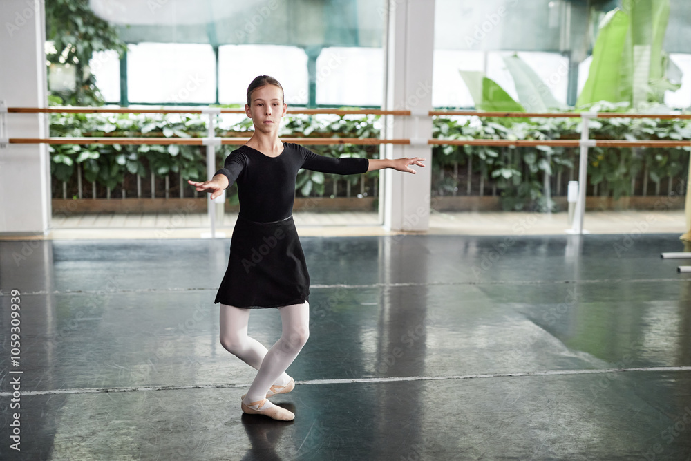 Full length shot of concentrated young girl wearing black dress for dancing getting ready to perform series of pirouettes while practicing ballet moves in dance studio with green plants, copy space Full length shot of concentrated young girl wearing black dress for dancing getting ready to perform series of pirouettes while practicing ballet moves in dance studio with green plants, copy space