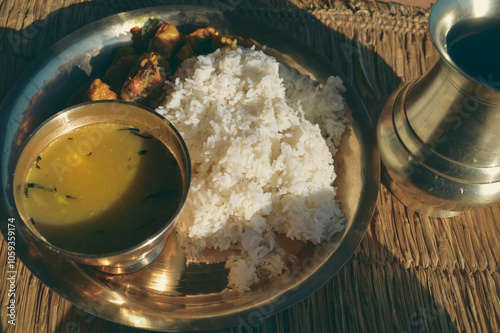 Dal bhat which is rice with lentil soup and chicken curry served on a brass plate known as chares or kaas ko thaal on a rustic straw mat showing the authentic traditional local nepali daily food