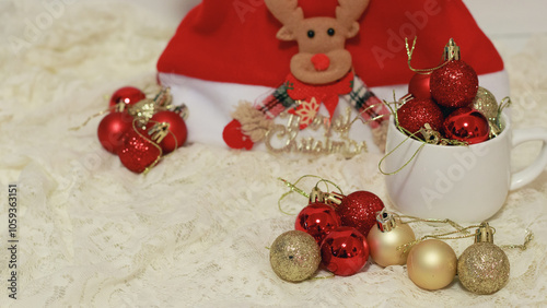 Red and gold Christmas baubles on a mug and reindeer ornament santa claus hat arranged on lace fabric depicting the festive mood of the holiday season