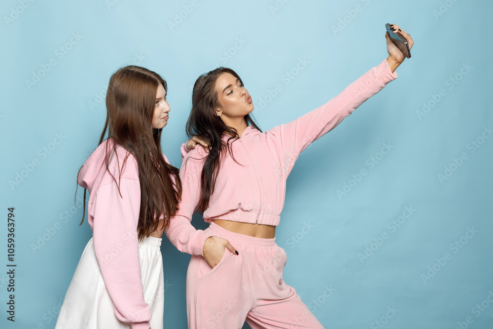 Two Friends Take a Playful Selfie While Wearing Matching Pastel Outfits Against a Blue Backdrop Two Friends Take a Playful Selfie While Wearing Matching Pastel Outfits Against a Blue Backdrop