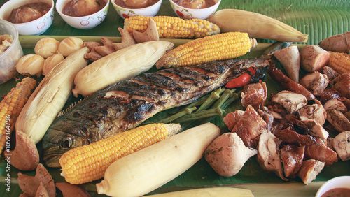 A close-up view of a traditional Filipino sharing meal called boodle fight with grilled fish, chicken corn, and assorted vegetables served on a banana leaf