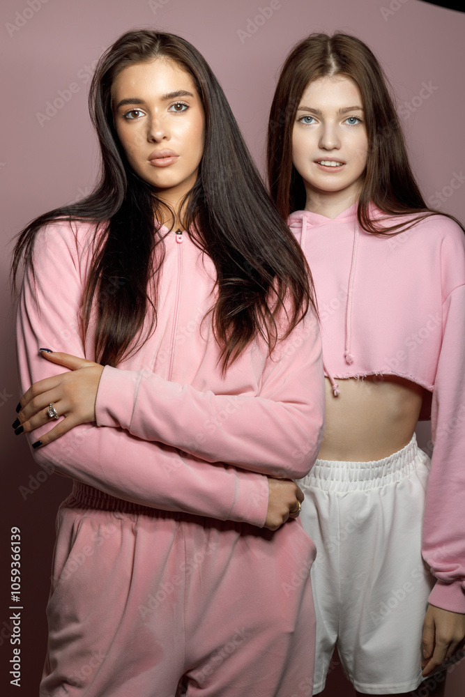 Two Young Women in Stylish Pink Outfits Posing Against a Soft Pink Backdrop Indoors Two Young Women in Stylish Pink Outfits Posing Against a Soft Pink Backdrop Indoors