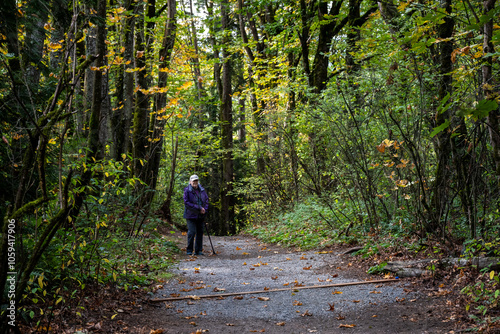 Senior woman with a walking stick getting fresh air on a gravel trail on a sunny fall day in the woods in Kirkland’s Watershed Park
