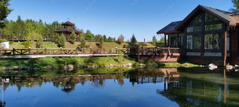 A tranquil cabin sits beside a clear lake, surrounded by lush trees and greenery. The scene captures beautiful reflections on the water under a bright sky. A tranquil cabin sits beside a clear lake, surrounded by lush trees and greenery. The scene captures beautiful reflections on the water under a bright sky.