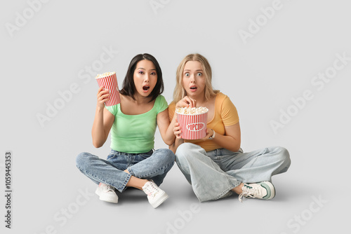 Emotional young women with buckets of popcorn on white background