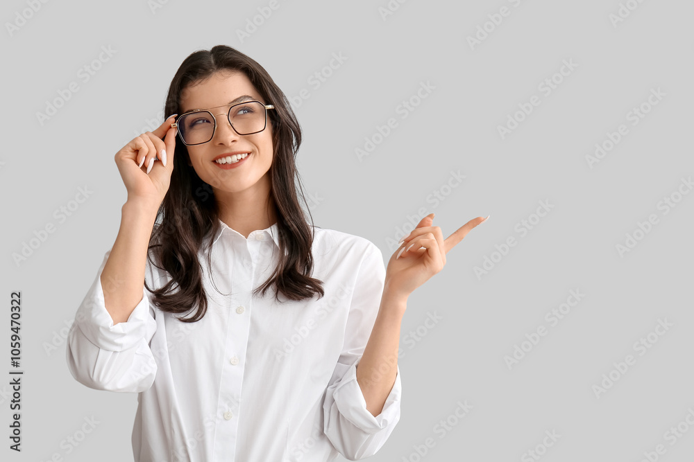 Happy smiling young woman in eyeglasses pointing at something on white background Happy smiling young woman in eyeglasses pointing at something on white background