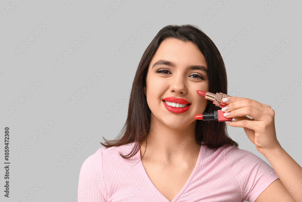 Beautiful young woman with lipsticks on grey background Beautiful young woman with lipsticks on grey background