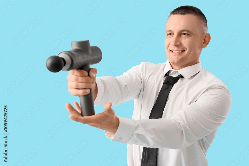 Young businessman with percussive massager on blue background Young businessman with percussive massager on blue background