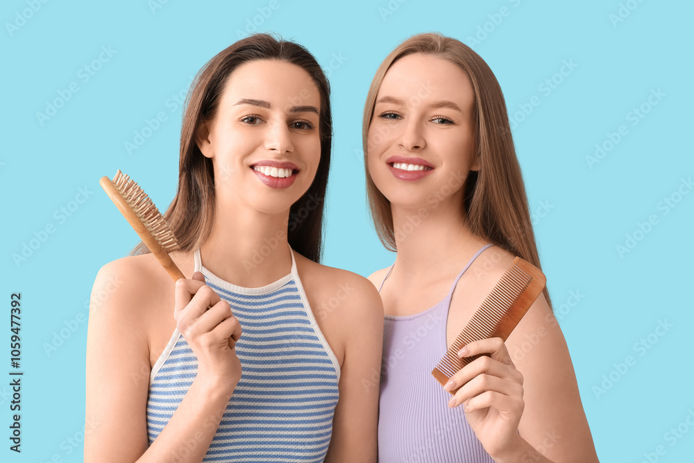 Beautiful young sisters with brush and comb on blue background Beautiful young sisters with brush and comb on blue background