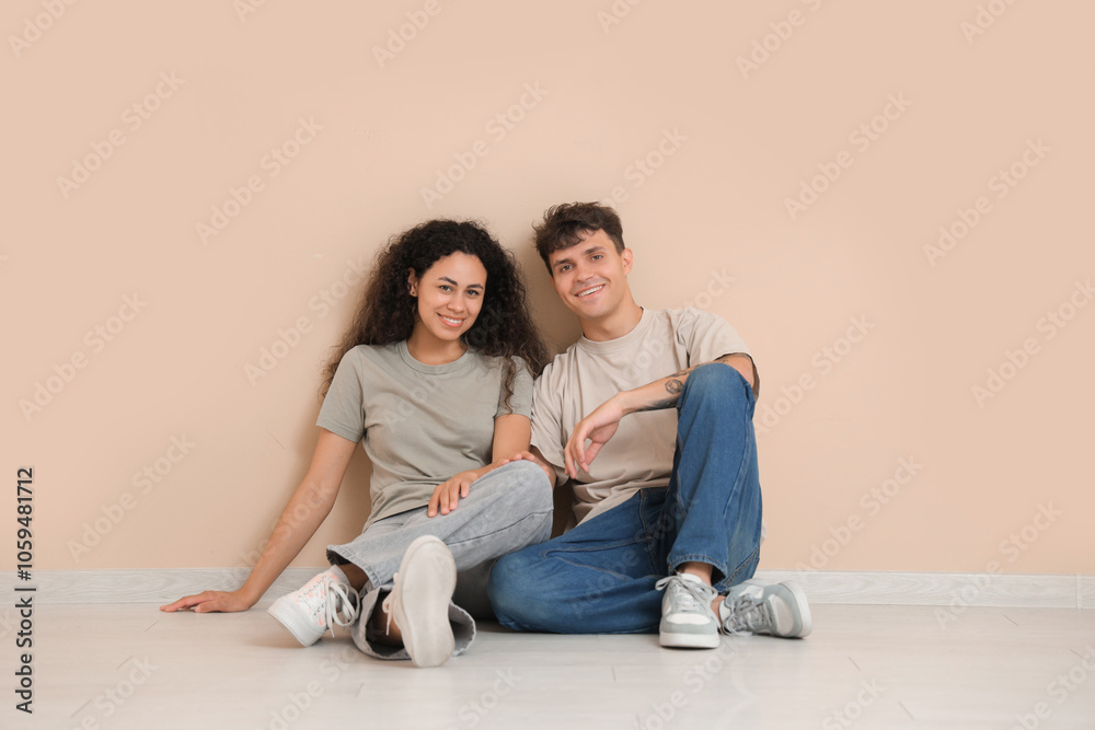 Young couple sitting on floor near beige wall in their new flat Young couple sitting on floor near beige wall in their new flat