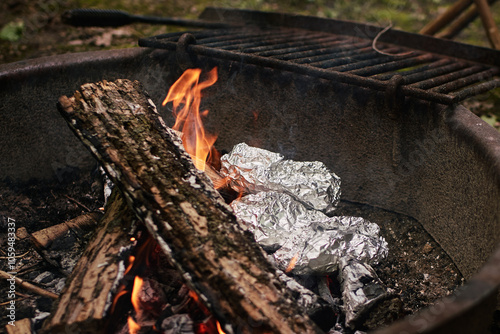 Foil-wrapped meals cooking in campfire flames
