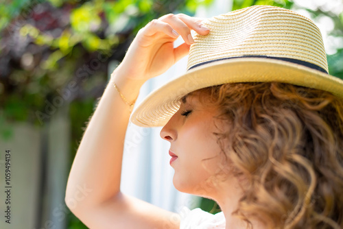 nachdenkliche junge Frau mit Strohhut geniesst die Sonne im Garten