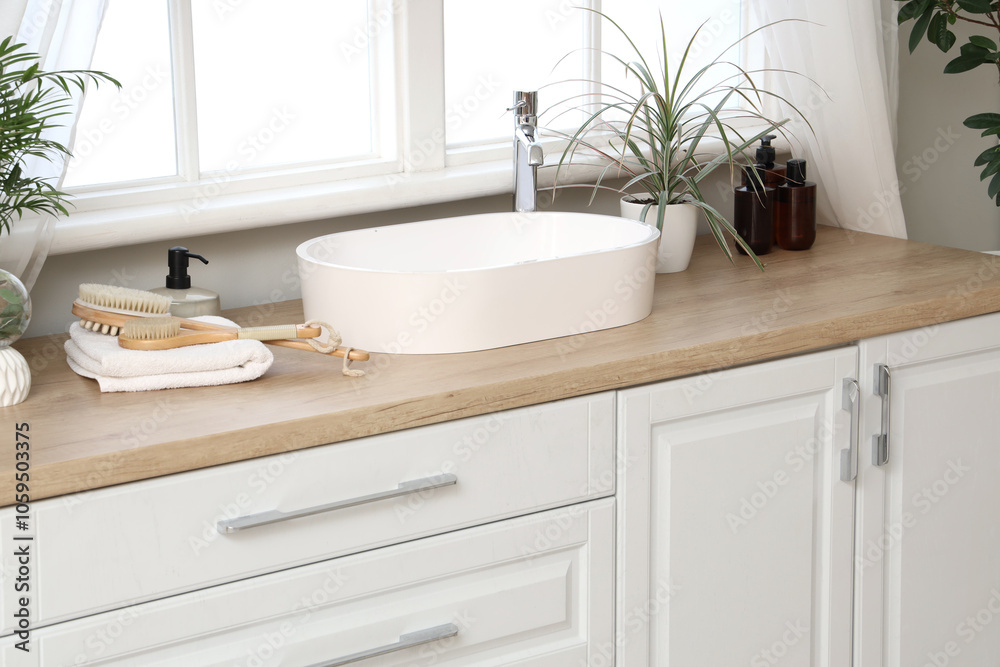 Fototapeta premium Modern sink, towels and massage body brushes on chest of drawers near window in bathroom