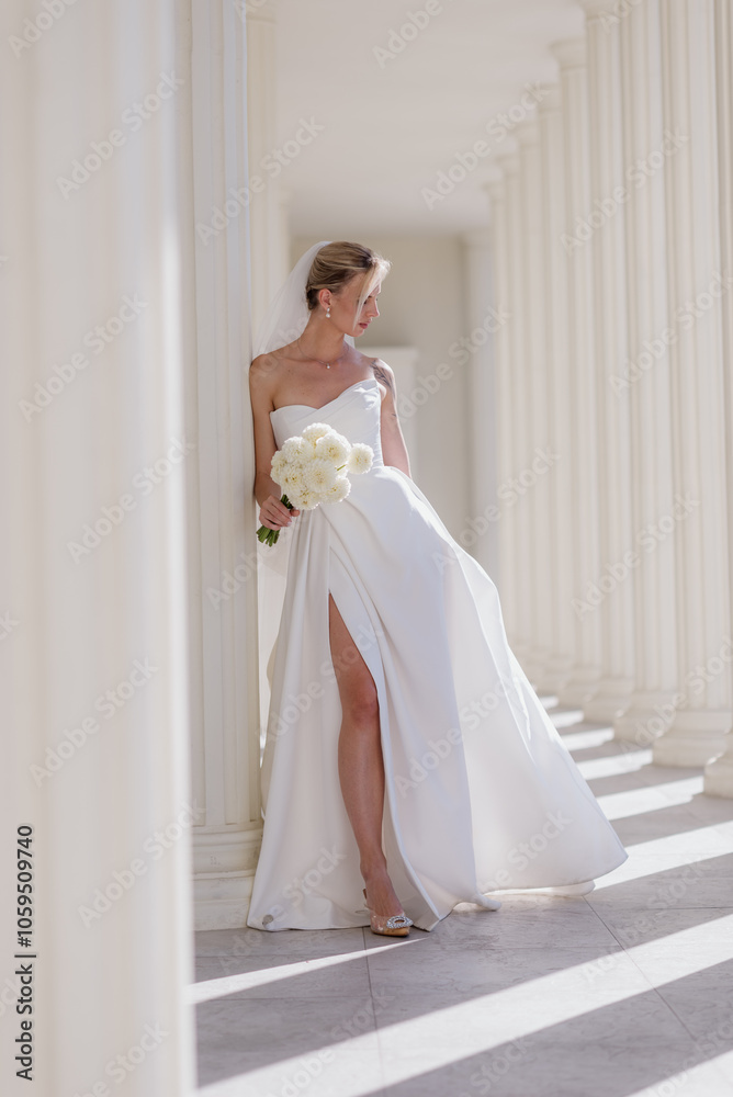 Fototapeta premium A beautiful bride in a white dress with a bouquet of white flowers on a light background. The year of the family. Marriage