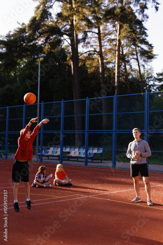 Schoolboy making jump shot on court under supervision of trainer photo