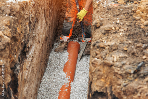 Φωτογραφία Construction worker installing drainage pipe in a trench during daylight, surrou