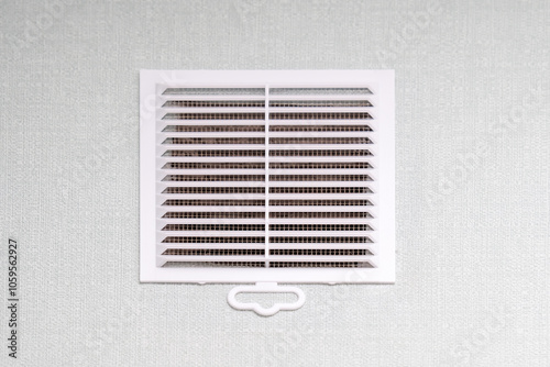A rectangular white air vent is hanging on an equally white wall