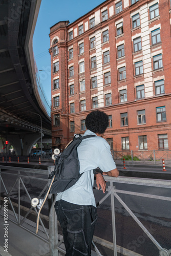 Man with Backpack and Skateboard Facing Brick Building