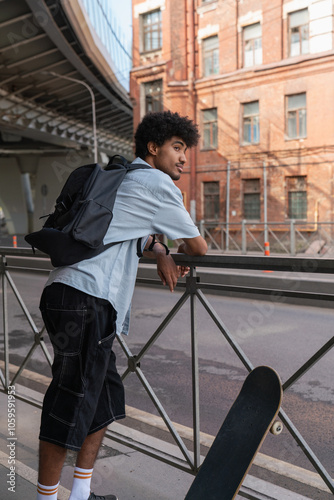  Young man leaning on railing with skateboard in urban area