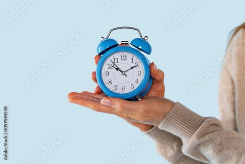 A woman's hand holds a vintage blue alarm clock, symbolizing the importance of time management and punctuality