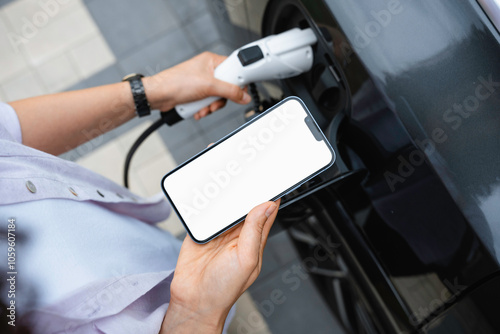 A woman uses a mobile phone standing near an electric car photo