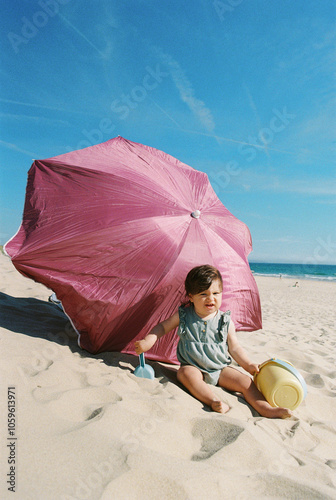 Baby sitting on the sand against pink parasol on the beach photo