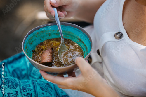 Person enjoying hearty lentil soup with sausage in a vibrant blue bowl photo