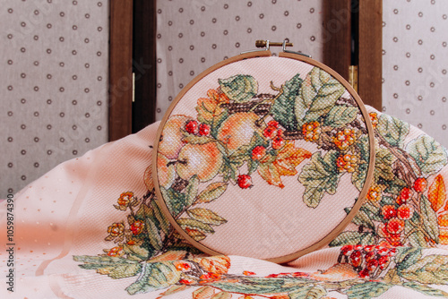 An embroidery hoop with a bright floral pattern is shot close-up against a pale pink background. Do-it-yourself aesthetic installation. photo