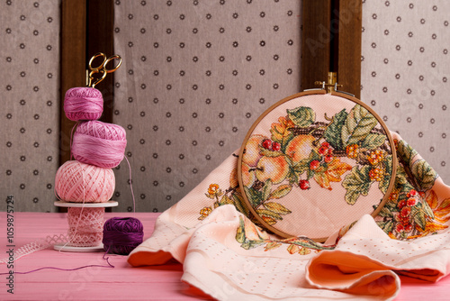 Delicate embroidery with floral patterns and pink threads conveys the essence of traditional needlework. Knitting threads and scissors lie on the table nearby. photo