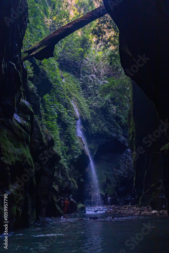 Billede på lærred Mysterious Jungle Waterfall Flowing Through Narrow Canyon with Lush Greenery
