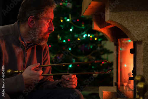 Man sits in front of burning fireplace. Behind Christmas tree photo