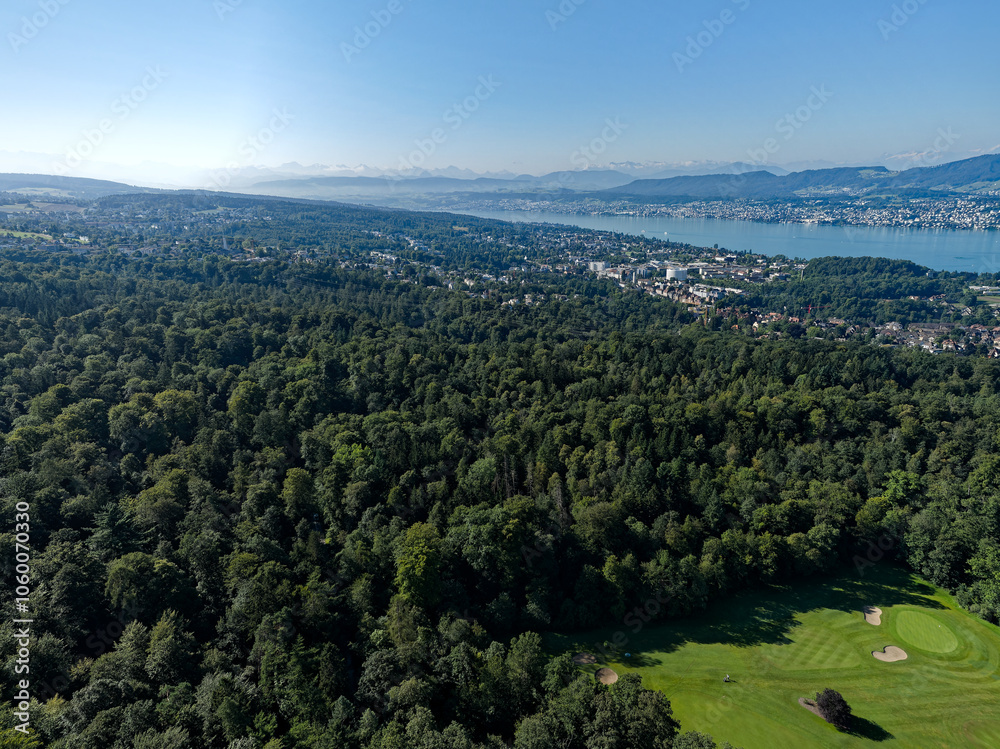 Fototapeta premium Aerial view of Swiss City of Zürich with Lake Zürich and cityscape and golf course in the foreground on a sunny summer morning. Photo taken July 6th, 2024, Zurich, Switzerland.