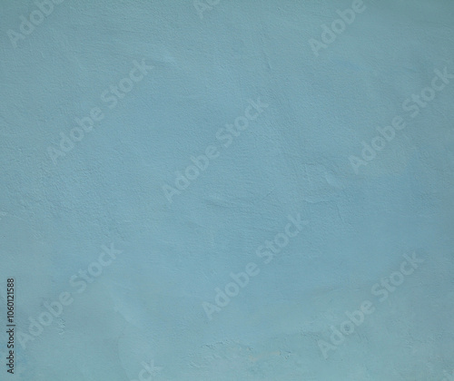 Blue or dark-blue wall, texture, background. The building wall, painted with water-based paint. Pale (flat) surface and backdrop in soft blue color. Flat surface with small dents and unevenness