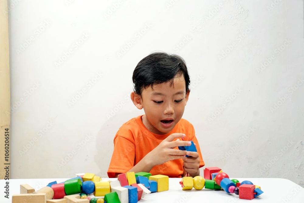 A young boy in an orange shirt focused on stringing colorful wooden beads, developing fine motor skills and creativity. Ideal for educational, childhood development, and playful learning concepts. A young boy in an orange shirt focused on stringing colorful wooden beads, developing fine motor skills and creativity. Ideal for educational, childhood development, and playful learning concepts.