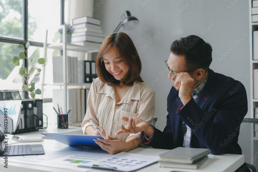Two asian coworkers are discussing and working together using a digital tablet and looking at paperwork with graphs and charts Two asian coworkers are discussing and working together using a digital tablet and looking at paperwork with graphs and charts
