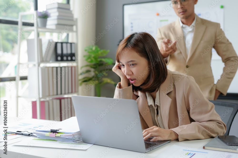 Stressed businesswoman looking at laptop screen with worried expression while her boss is scolding her for bad results in modern office Stressed businesswoman looking at laptop screen with worried expression while her boss is scolding her for bad results in modern office