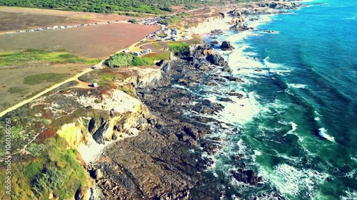 Rotating drone view of Praia da Samoqueira Beach and seaside highway with parked cars photo