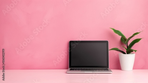 A minimalist workspace featuring a laptop and a potted plant against a pink wall, creating a vibrant and modern aesthetic.