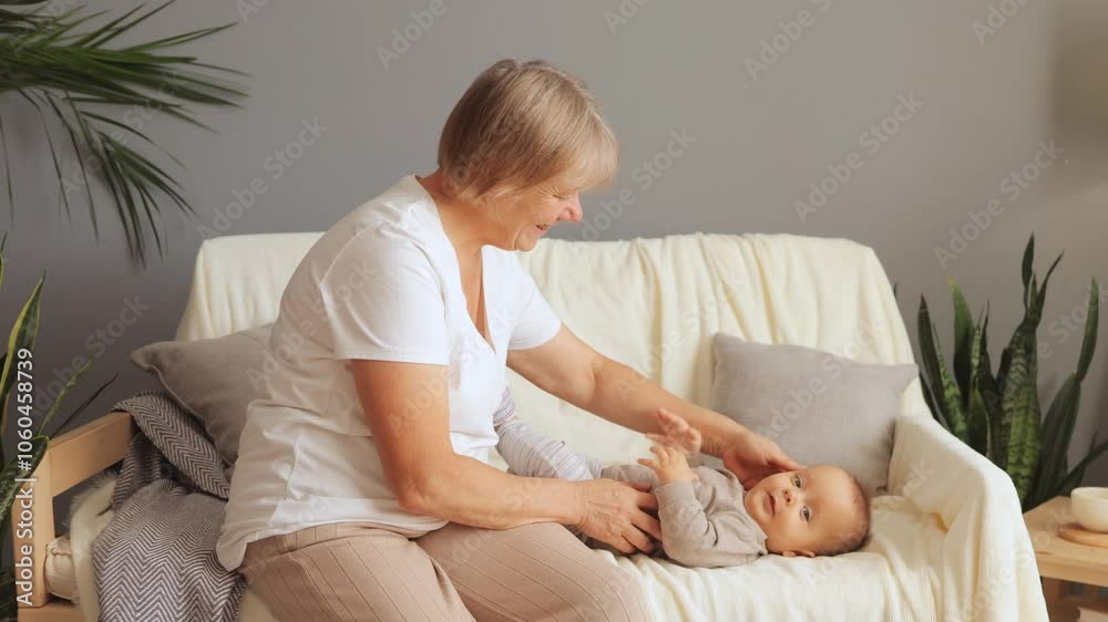 Smiling senior woman bonding with her baby grandson enjoying precious moments together loving grandmother looking after infant grandchild sitting on sofa at home Smiling senior woman bonding with her baby grandson enjoying precious moments together loving grandmother looking after infant grandchild sitting on sofa at home