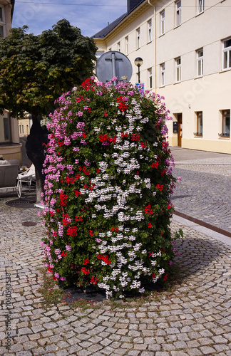 Fototapeta Naklejka Na Ścianę i Meble -  Decorative flower column in small town square. Flower decoration in the streets of the city. Flowers, blossoms, plant, summer, season.