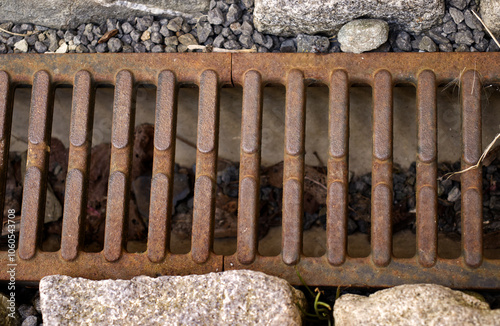 Iron grating on the drainage channel. Iron grating on the ground. Rust on iron, stones, ground, drain. photo