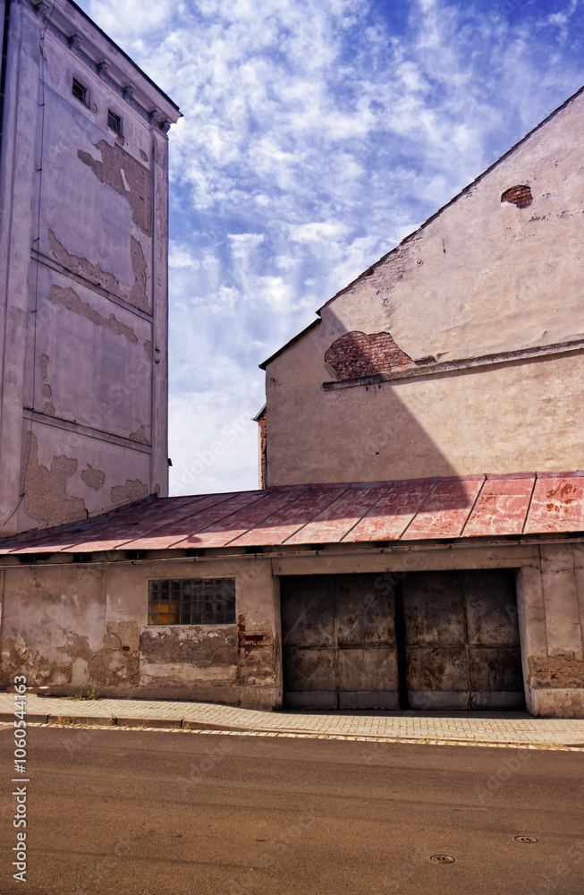 A street with a concrete road and a low building with a wide iron gate. Street, road, houses. City. A low building with luxfers and a tin roof. A street with a concrete road and a low building with a wide iron gate. Street, road, houses. City. A low building with luxfers and a tin roof.