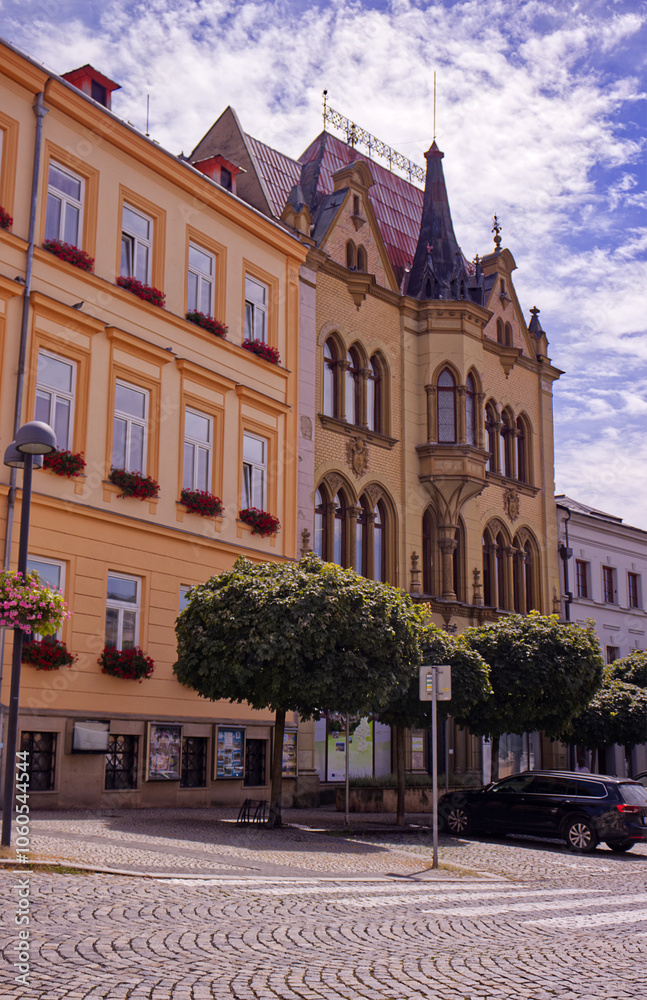 Naklejka premium Square with Historic building with decorative elements. Paved square with trees in front of buildings and parked cars.