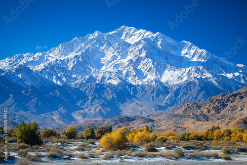 Snow-capped mountains rise majestically under a clear blue sky surrounded by vibrant autumn foliage during a sunny day