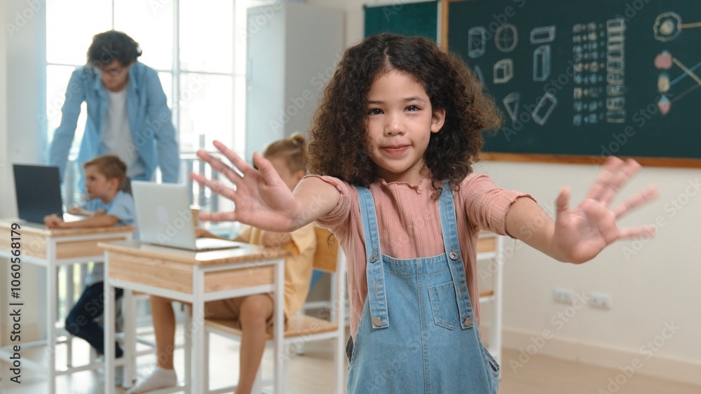 American girl looking at camera while waving hand to greeting. Group of diverse elementary student studying coding engineering prompt and generating AI or programing software. Education. Pedagogy. American girl looking at camera while waving hand to greeting. Group of diverse elementary student studying coding engineering prompt and generating AI or programing software. Education. Pedagogy.