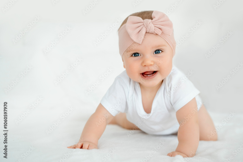 A baby girl is smiling at home on a white bed with a bow on her head, a happy healthy child of six months is laughing A baby girl is smiling at home on a white bed with a bow on her head, a happy healthy child of six months is laughing