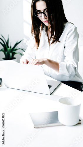 woman a white shirt glasses working on a laptop at her desk