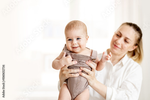 a young mother holds her little newborn baby at arm's length in the bedroom by the window, the mother's love and care for the child, mom and baby photo